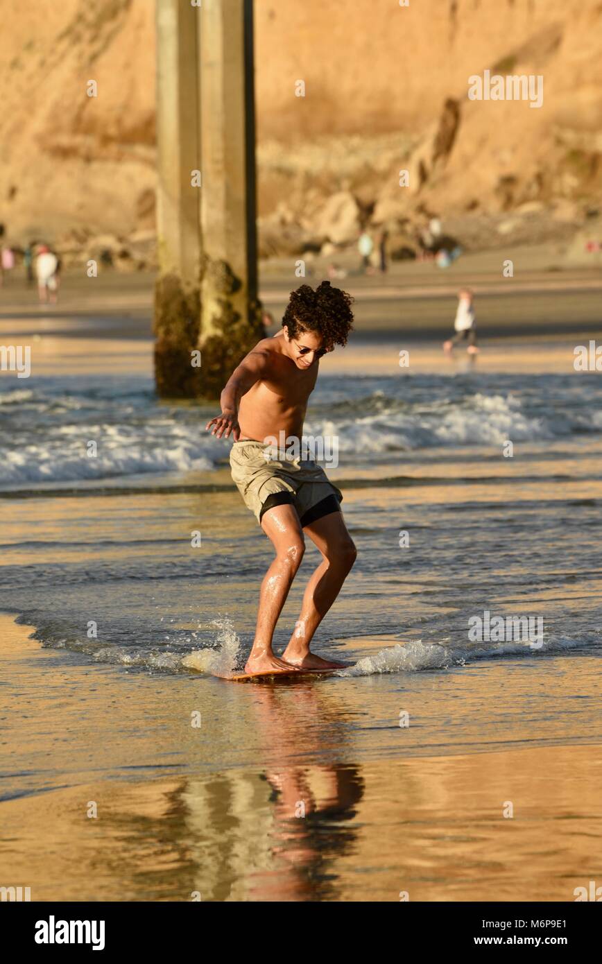 Young AfricanAmerican man on a skim board, skimming, at beach during