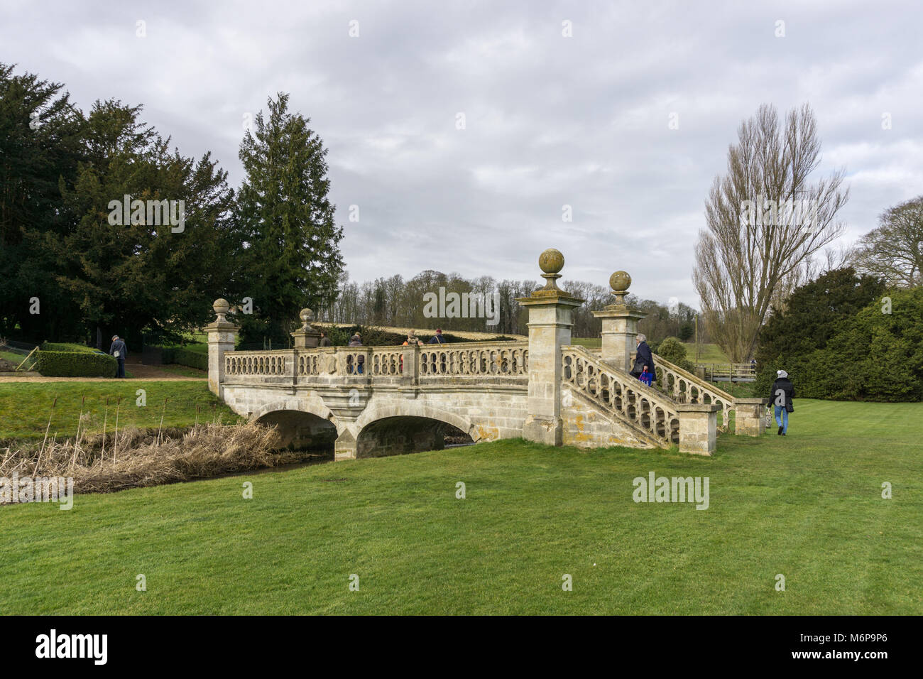 Easton Walled Gardens in winter, with visitors admiring the ornamental bridge; near Grantham, Lincolnshire, UK Stock Photo