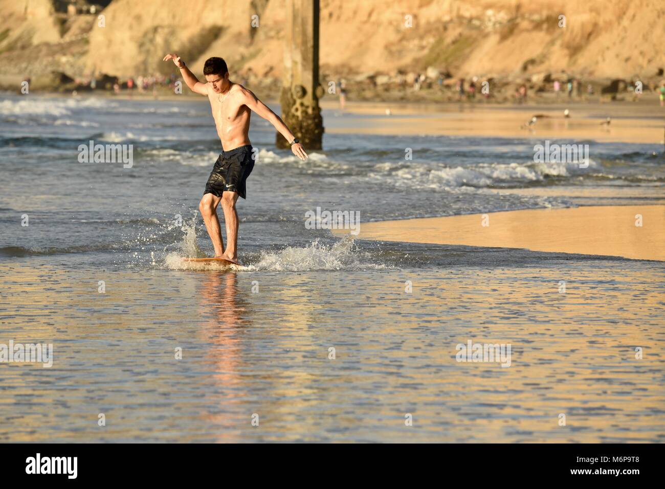 Young man on a skim board, skimming, at beach during sunset, gliding