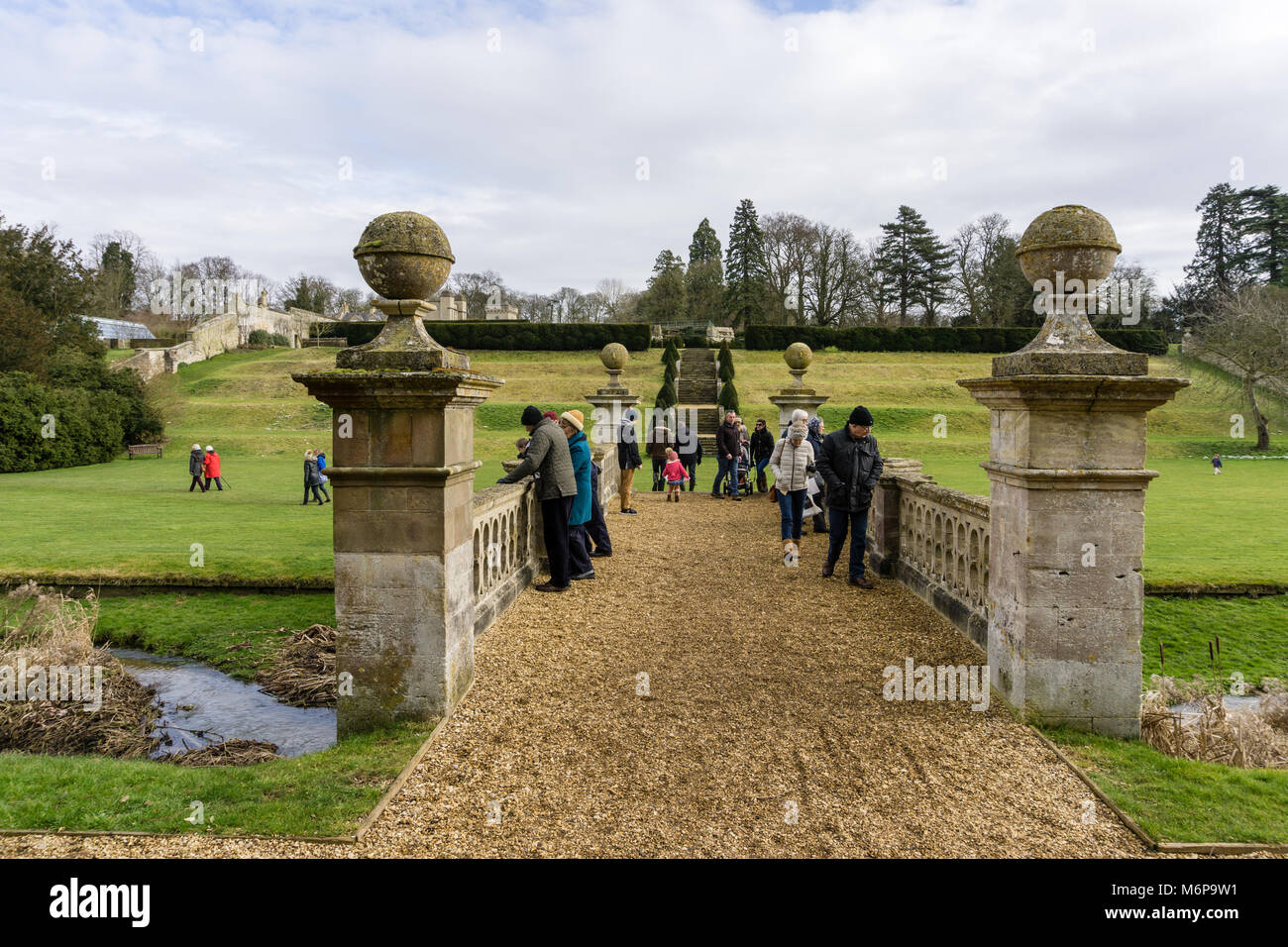 Easton Walled Gardens in winter, with visitors admiring the ornamental bridge; near Grantham, Lincolnshire, UK Stock Photo