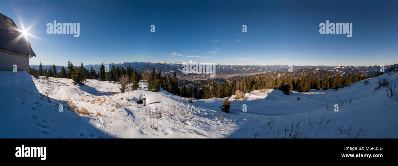 Wide panoramic landscape from snowy summit of mountain Rennfeld with hut and distant mountain tops in Winter Stock Photo