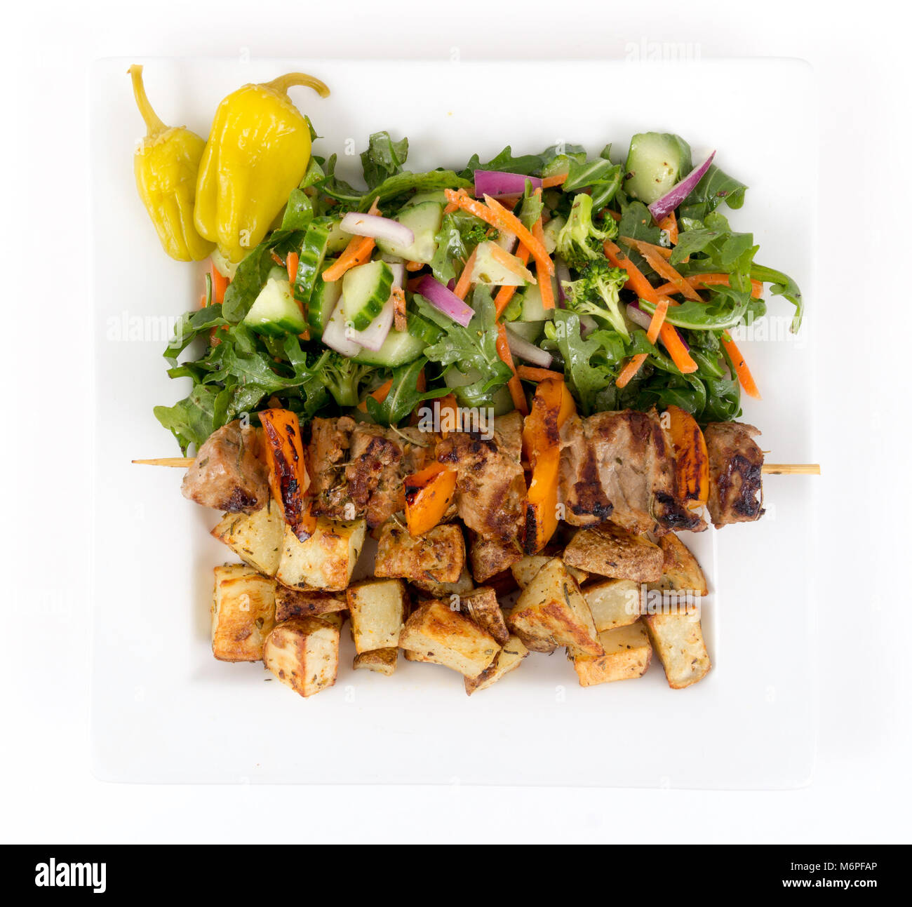 pork kebab skewer dish with potatoes and salad over white background