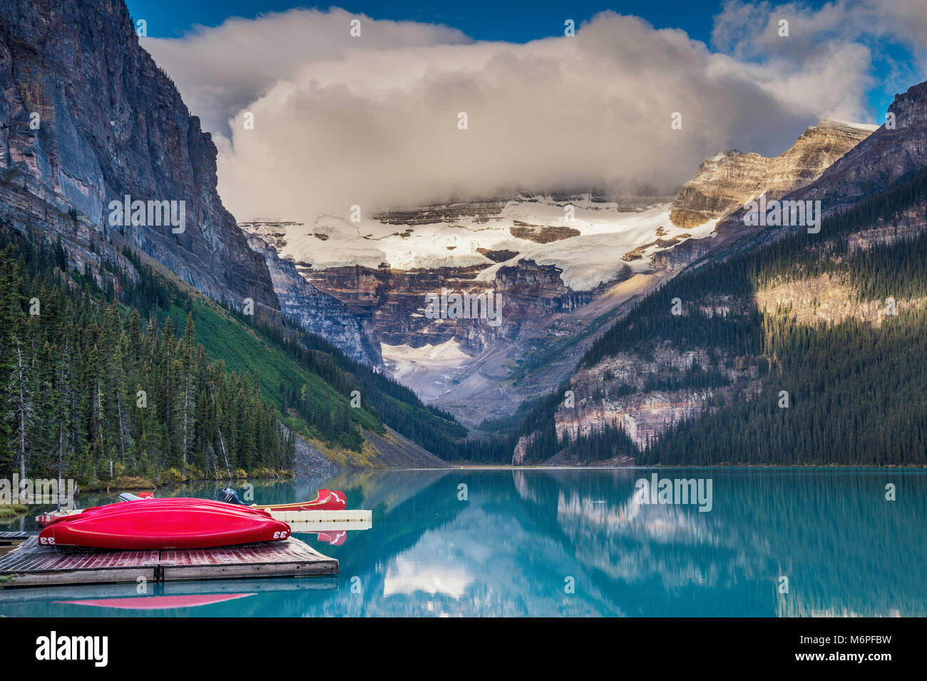 Mount Victoria in clouds over Lake Louise, red canoes on deck, Canadian Rockies, Banff National Park, Alberta, Canada Stock Photo