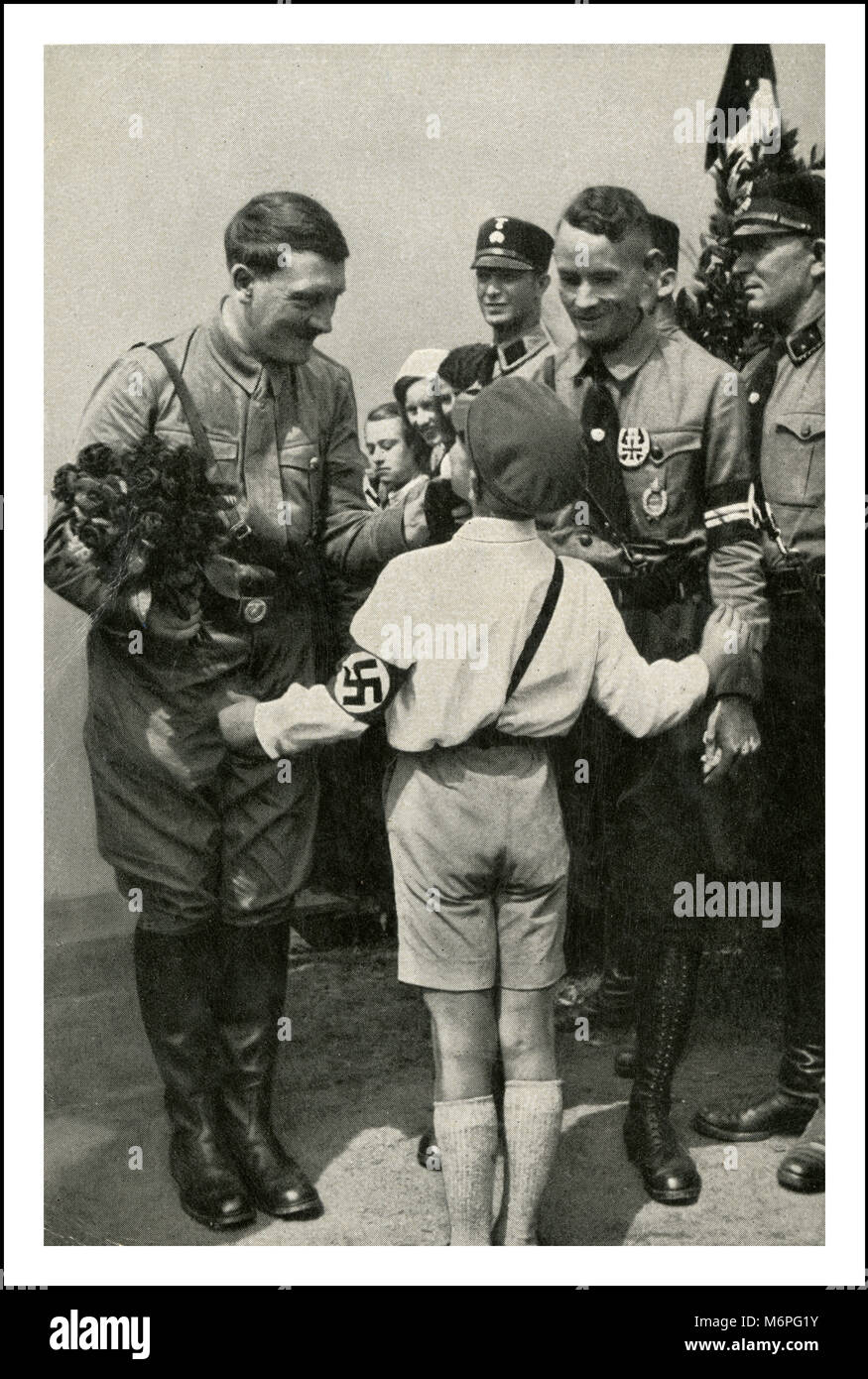 Pre WW2 1930’s Adolf Hitler holding flowers with NSDAP henchmen greeting young boy party member who is wearing a swastika armband Stock Photo