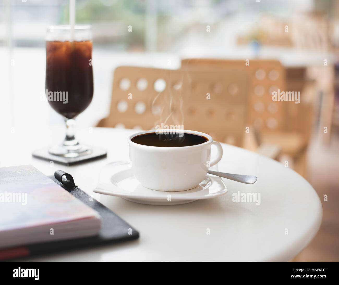 Hot black coffee mug on white table while still has a steam at empty cafe/restaurant. Concept of loneliness, isolation, abandonment or solitary. Stock Photo