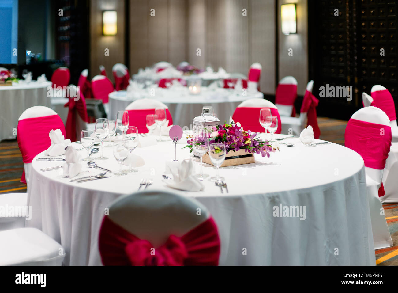 The wedding reception dinner table decorated with orchids, flowers, candle, White spandex chairs cover with red organza sash Stock Photo