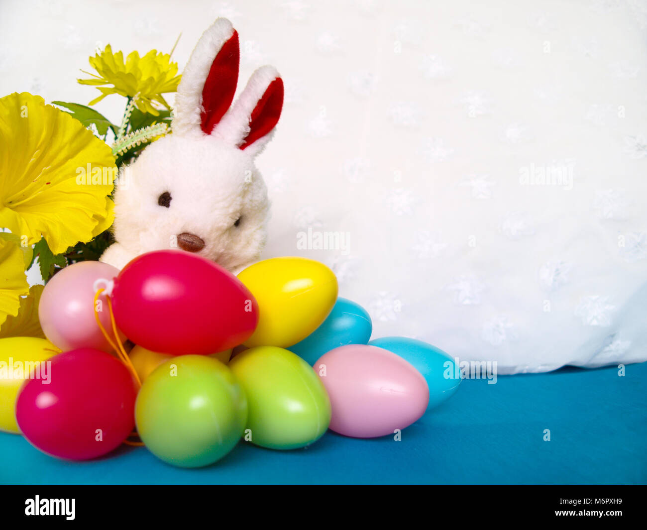 White plush rabbit with colorful Easter eggs and yellow flowers. Empty space for text. Stock Photo