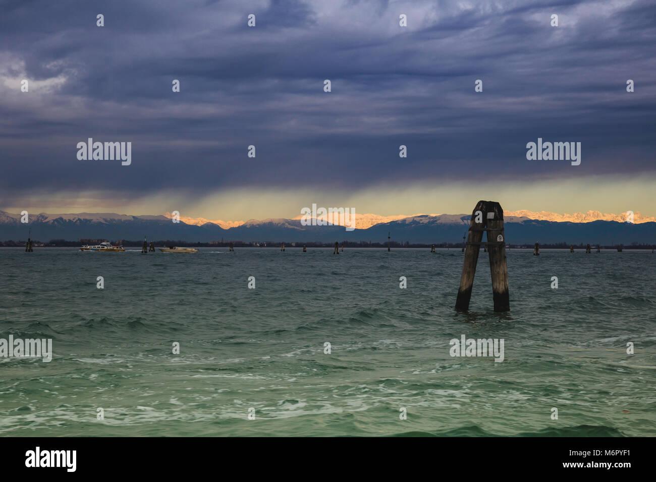 Venetian Laguna during a storm in the background of snowy Alps sunlit Stock Photo