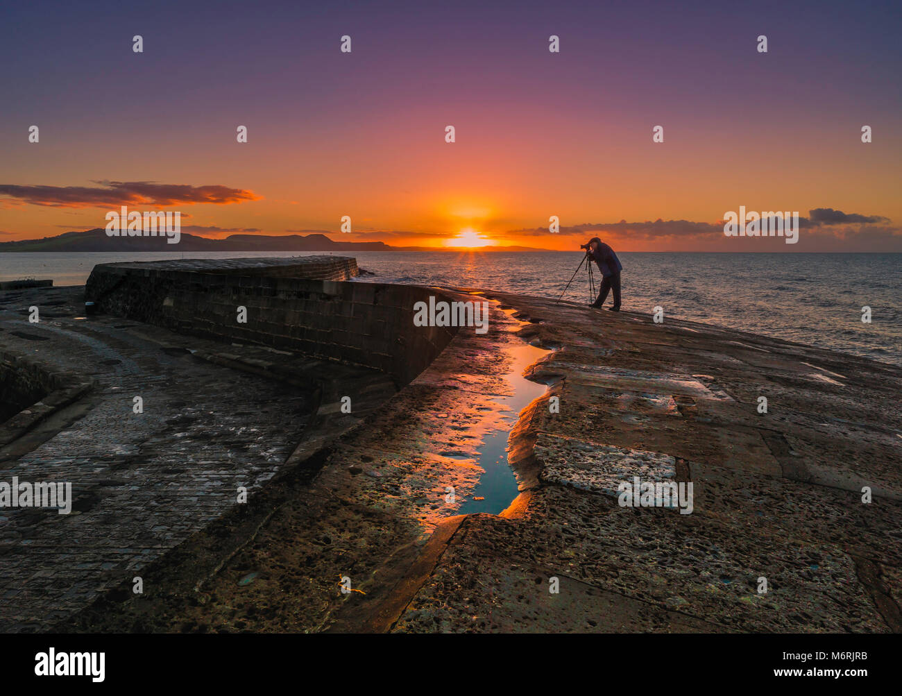 A photographer on The Cobb in Lyme Regis at dawn. Stock Photo