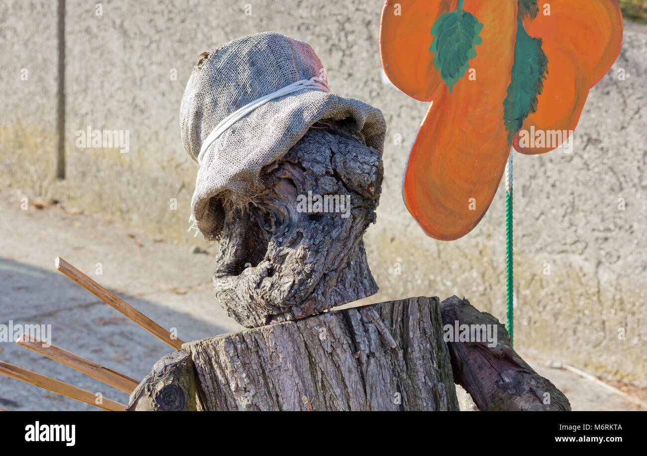Closeup of a wooden dummy made by pieces of a tree trunk holding a big painted orange flower Stock Photo
