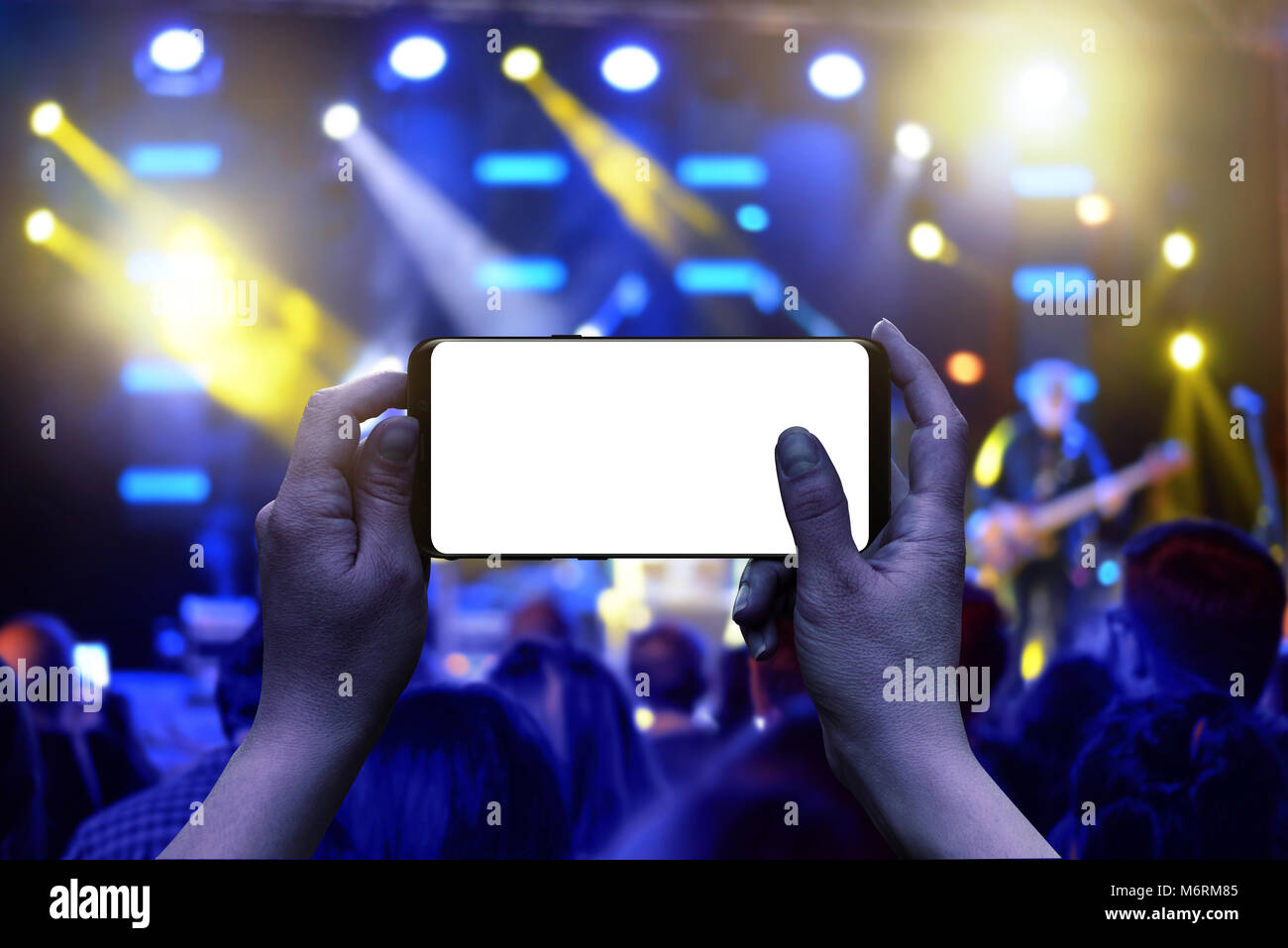 Mobile phone with isolated display in hands. Horizontal position. Live music concert in background. Crowd and lights. Stock Photo
