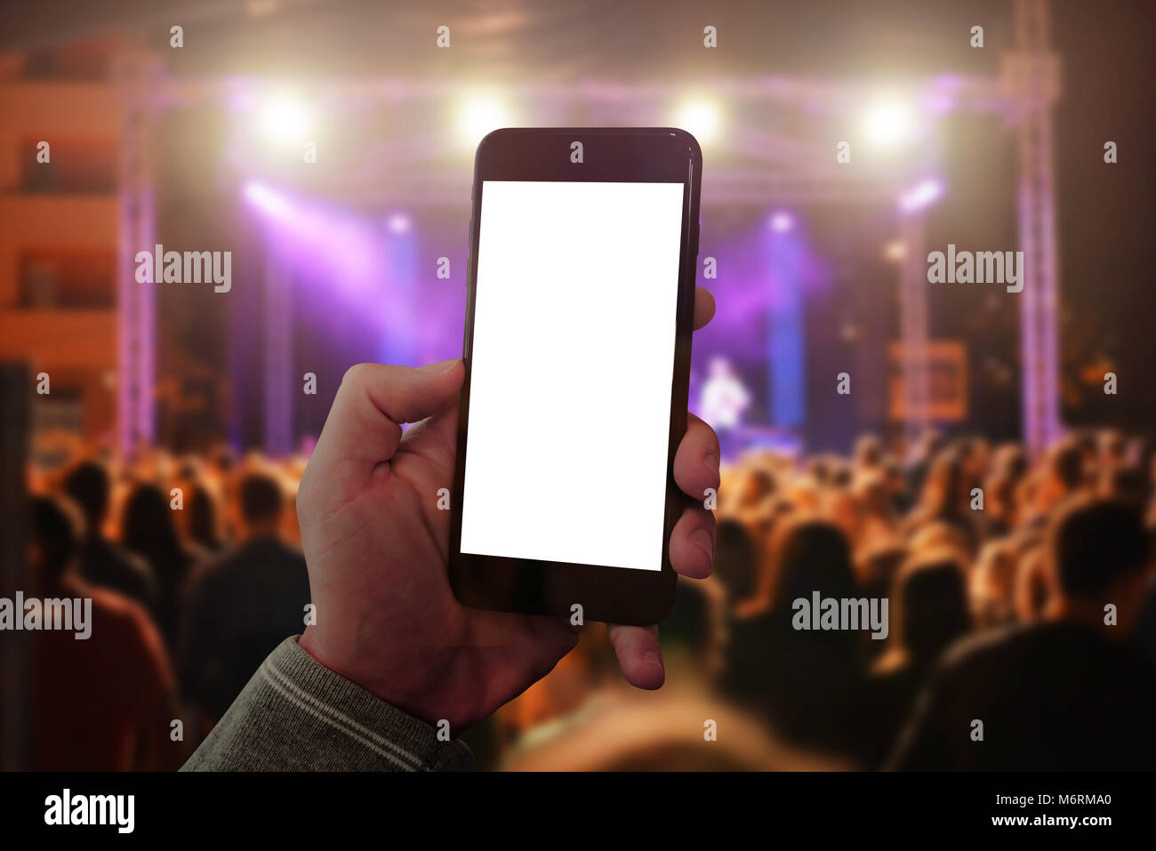 Man hand holding mobile smart phone and taking photo or video. Concert crowd and lights in background. Stock Photo