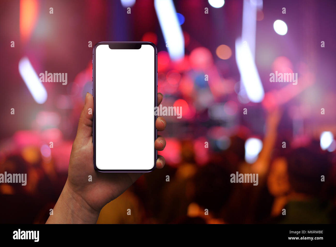 Modern mobile phone in woman hand with isolated screen for mockup. Live music concert and crowd in background. Stock Photo