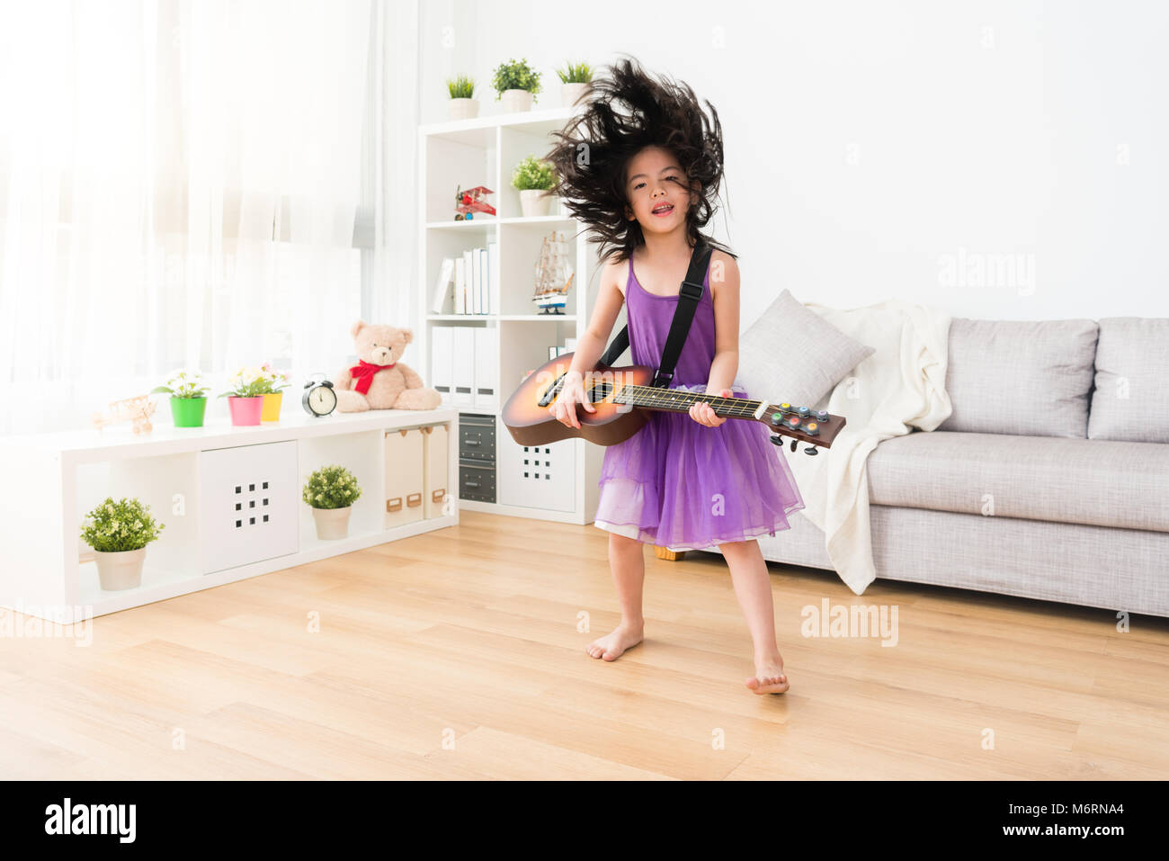 Crazy adorable asian girl playig the guitar and jumping in the living room. No one can stop her from playing the music. She enjoy it and full of passi Stock Photo