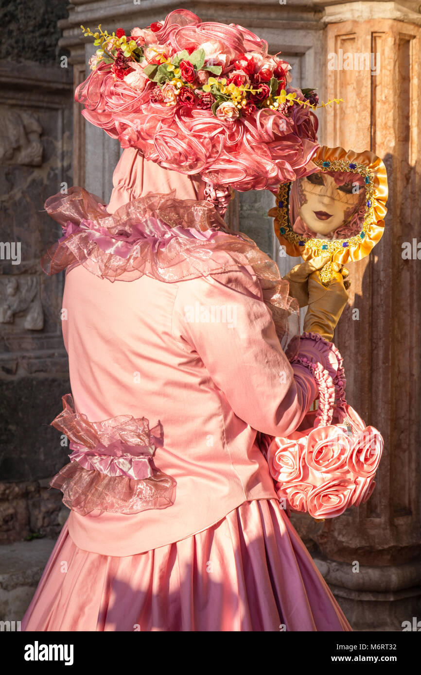Woman in pink beautiful fancy dress costume and mask holding mirror at