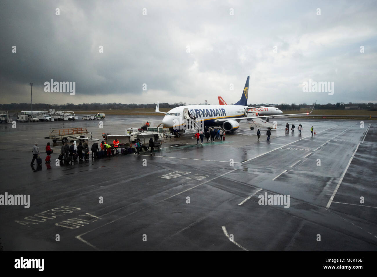 passengers dropping off luggage and boarding ryanair plane on the tarmac in the rain at belfast international airport Stock Photo