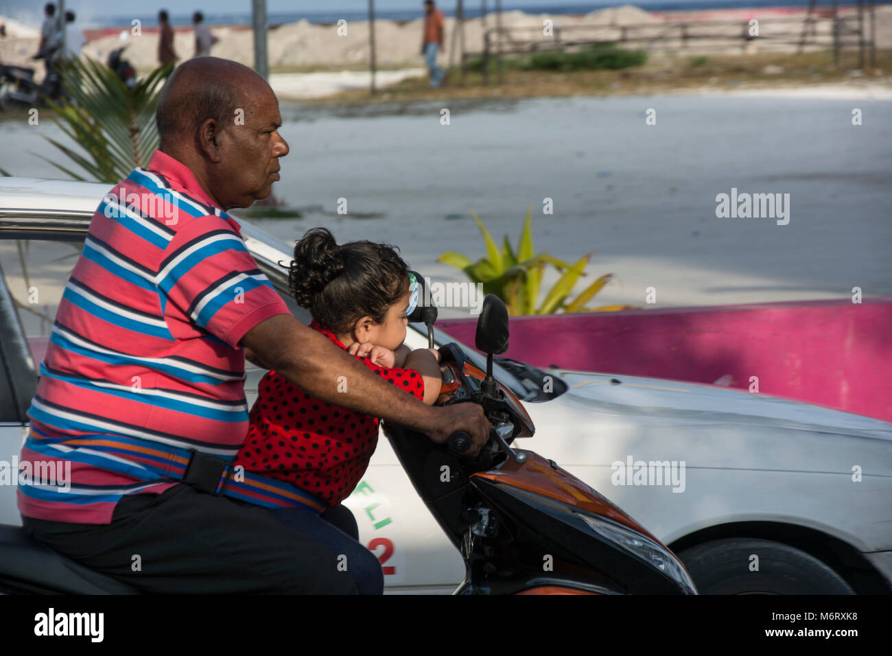 Malediver mit seiner kleinen Tochter auf dem Motorrad, eine übliche Art der Fortbewegung, Kinder sind mit Gurten am Fahrer fest. Stock Photo