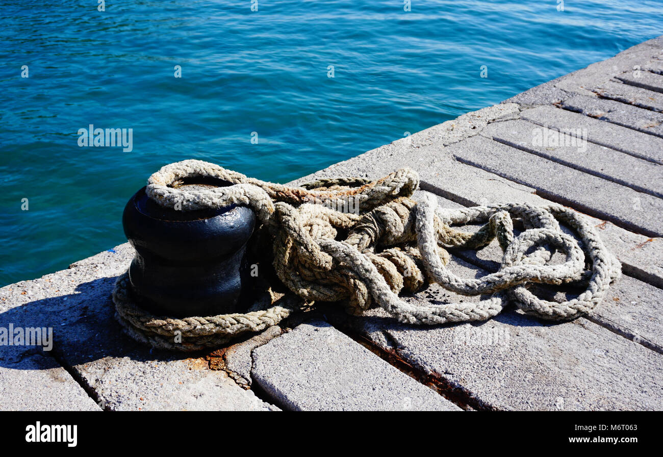 Dock with old knotted tied mooring rope near the blue sea Stock Photo