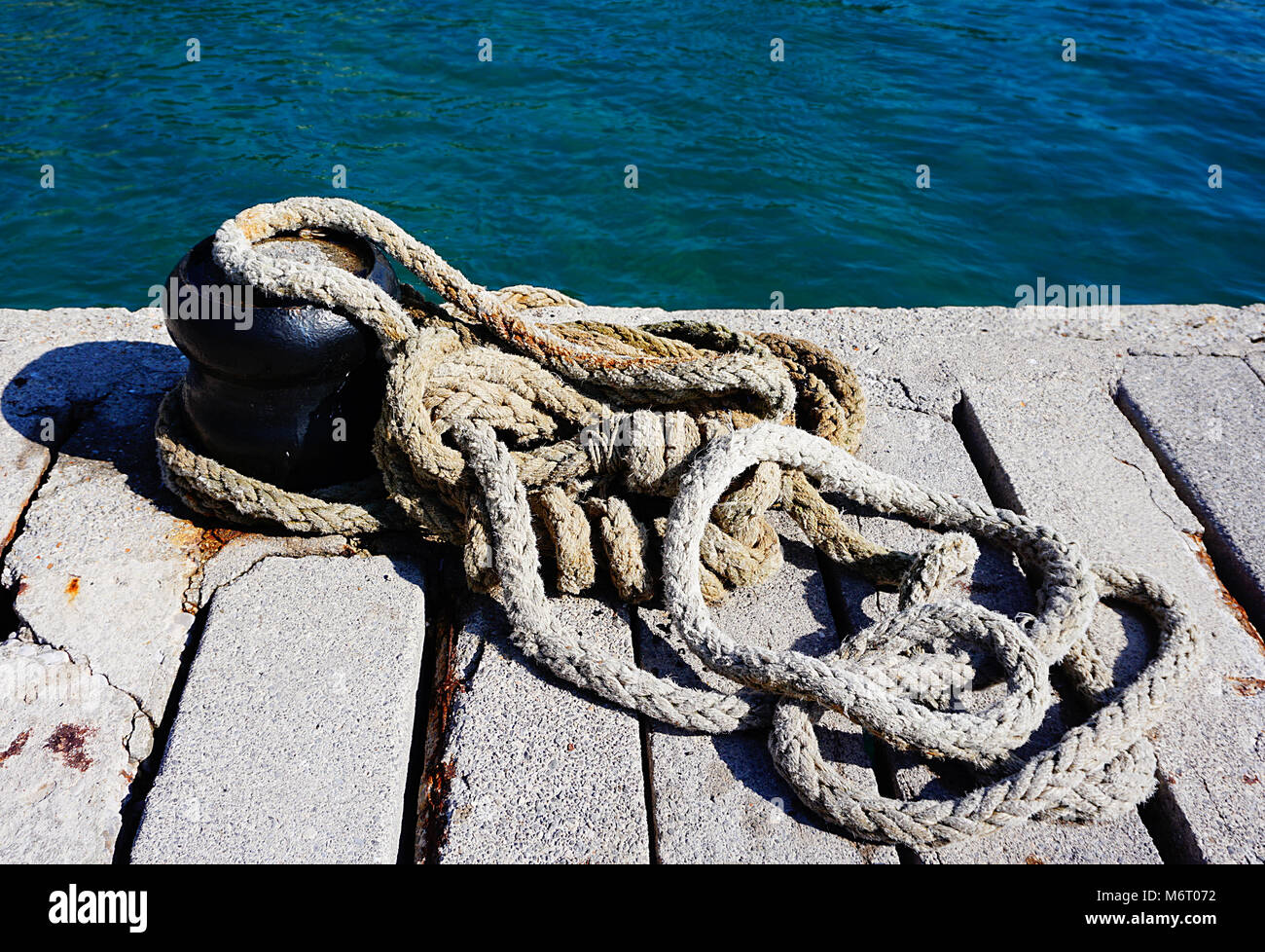 Old and rusty mooring rope on the marine dock near blue sea Stock Photo