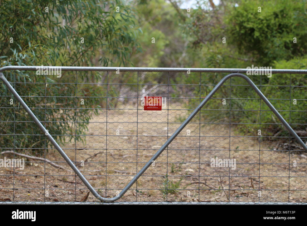 Farm gate on rural property, South Australia with 'Please Shut the Gate' sign. Gum and Wattle trees either side of dirt track behind Stock Photo
