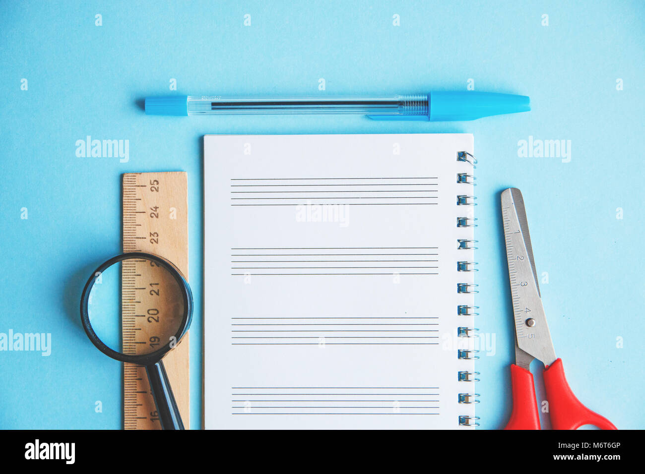 pen, ruler, magnifier and scissors on a blue background. Education or ...