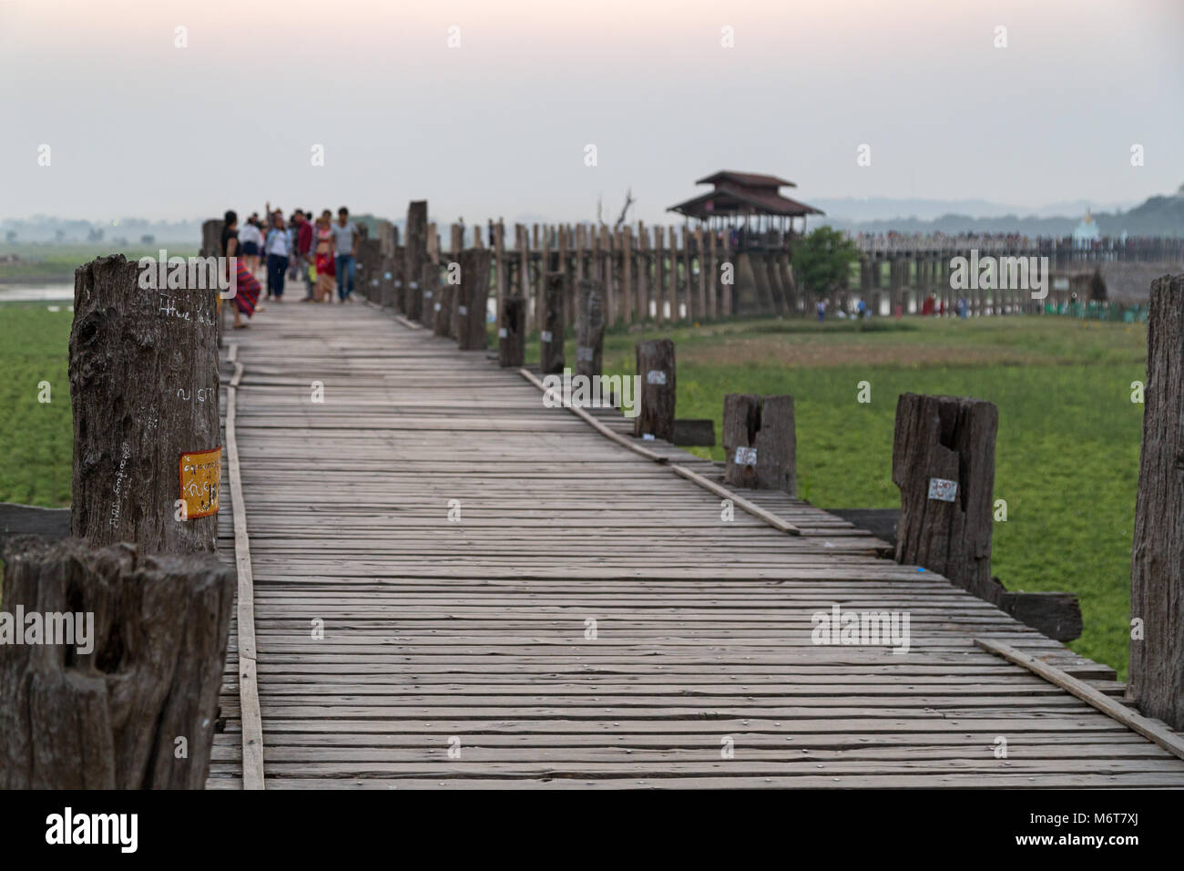 Some people at the U Bein Bridge at Amarapura near Mandalay in Myanmar. It's the oldest and longest teakwood bridge in the world.  Focus on foreground Stock Photo