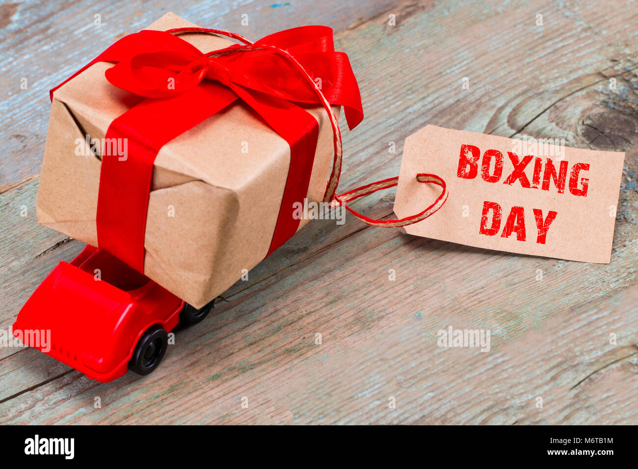 The BOXING DAY concept. Red toy car delivering gifts box with tag with  text: BOXING DAY on wooden background Stock Photo - Alamy
