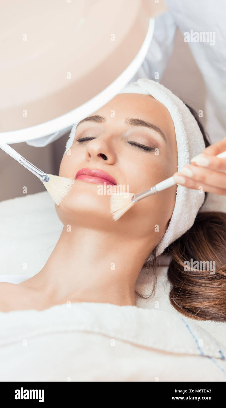 High-angle close-up view of the face of a beautiful woman during anti-aging facial massage with soft brushes in a modern cosmetic center Stock Photo