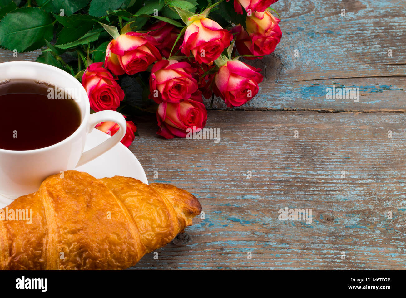 Cup of coffee with bouquet of roses  and croissant on a wooden background. Valentines, Mothers, Womens Day morning concept. Valentine's day breakfast. Stock Photo