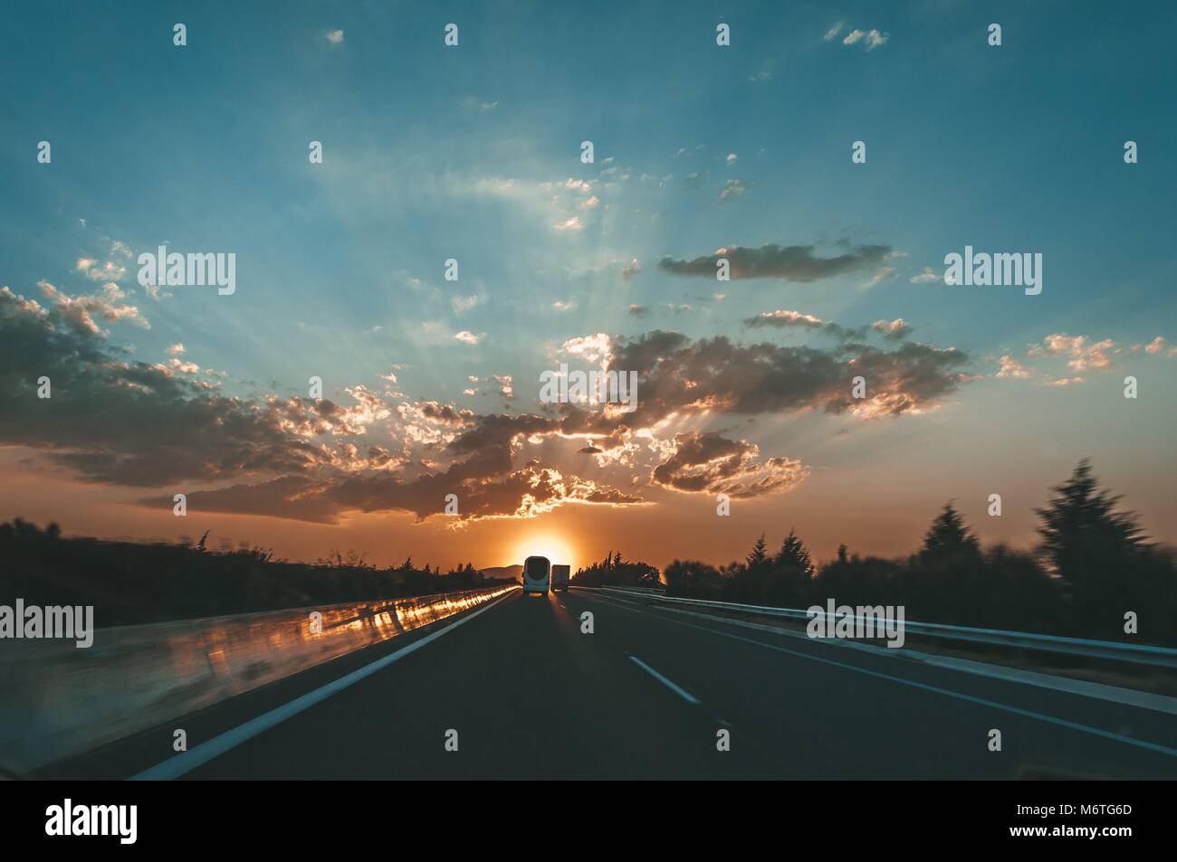 Colorful sunset over at highway. Landscape with orange sunset over highway. Cloud layers with sunrays between them. Contre-jour silhouette of cars. Stock Photo