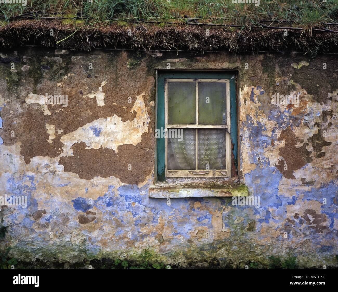 A decaying wall, window and grass roof of a rundown house in rural Ireland. Stock Photo