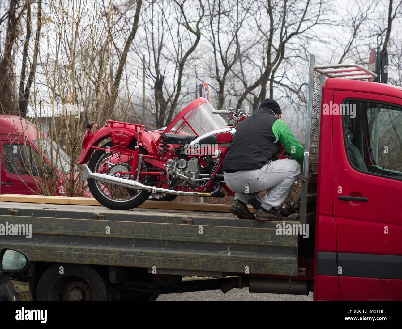 a worker firmly attaches a vintage motorcycle to the body of a transport van Stock Photo