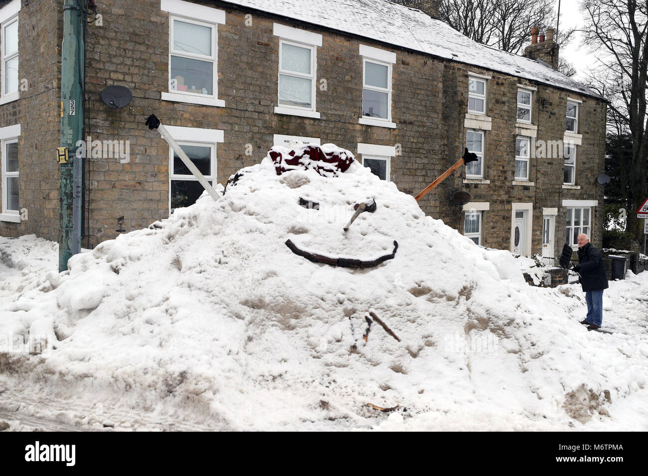A man stands by a giant snowman resembling Star Wars character Jabba the Hutt, built at St Johns Chapple in Weardale in County Durham. Stock Photo