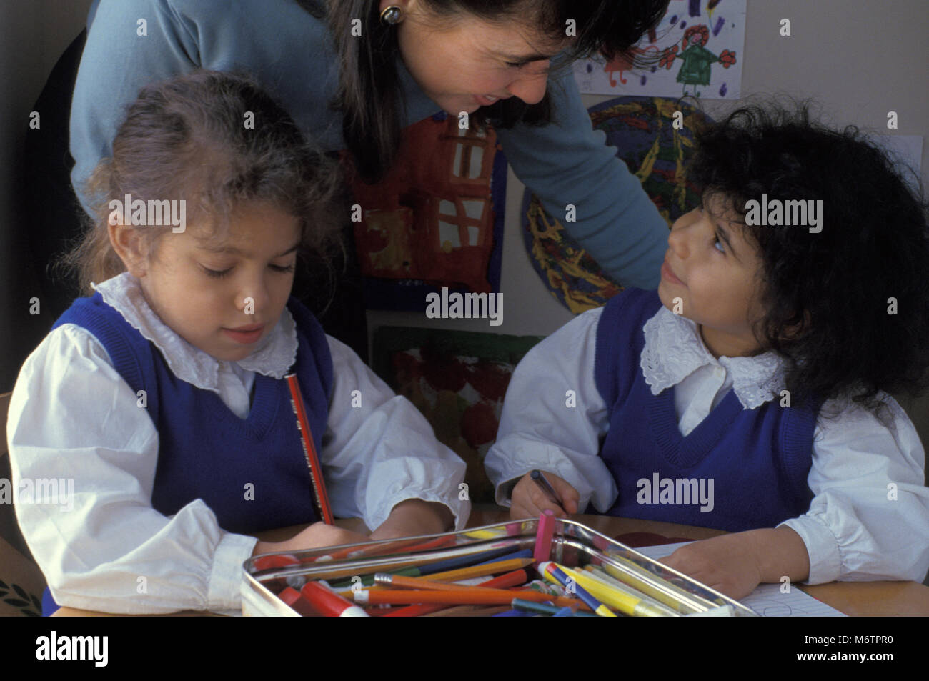 Two little girls with teacher or parent in classroom environment Stock Photo