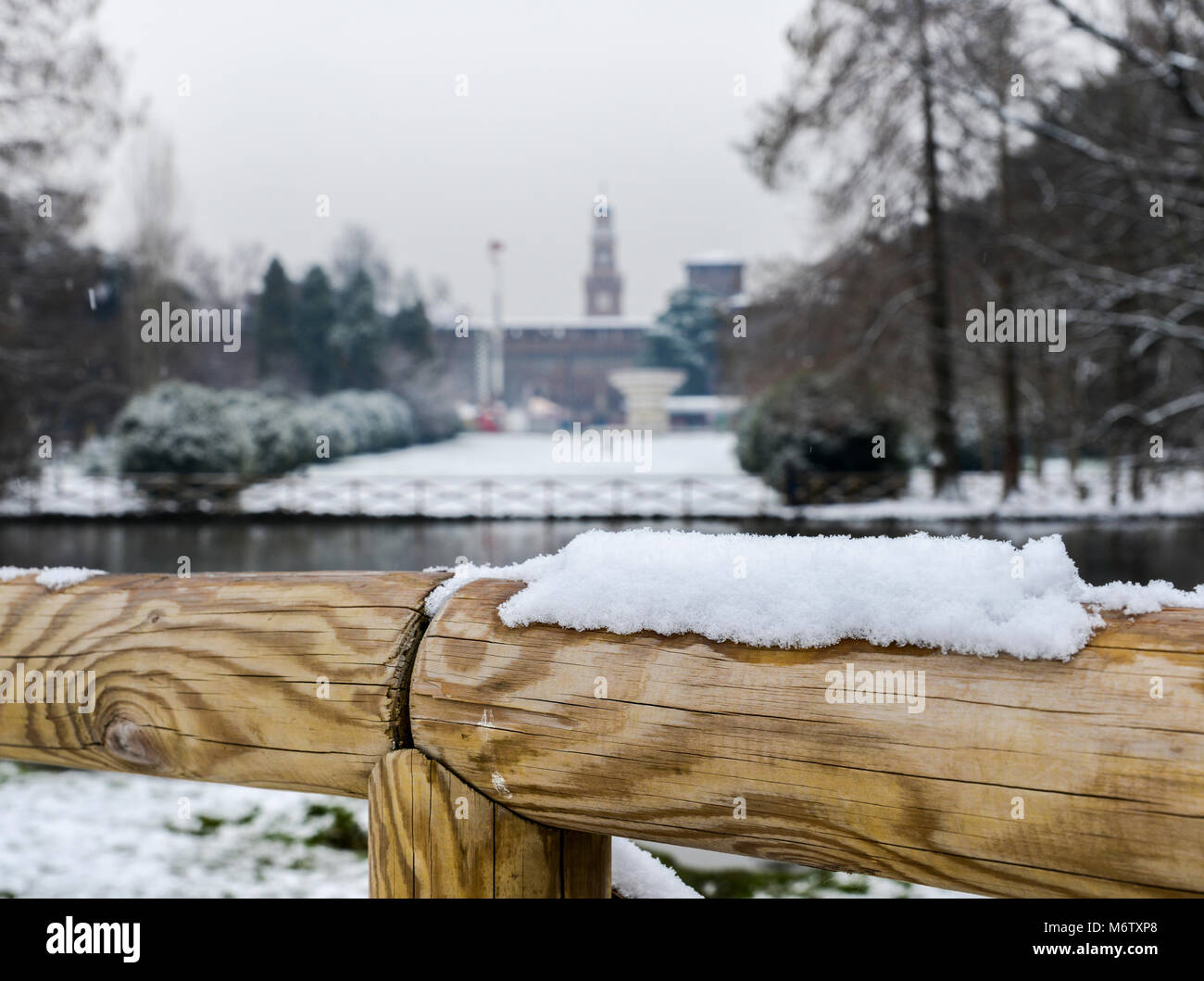 Selective focus of snow on wooden barrier with Sforza Castle, Italian: Castello Sforzesco, in Milan, northern Italy in background. Stock Photo