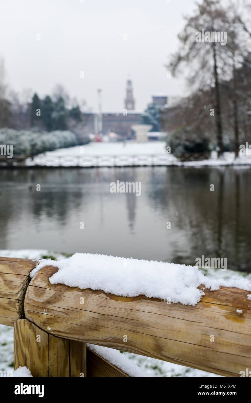Selective focus of snow on wooden barrier with Sforza Castle, Italian: Castello Sforzesco, in Milan, northern Italy in background. Stock Photo