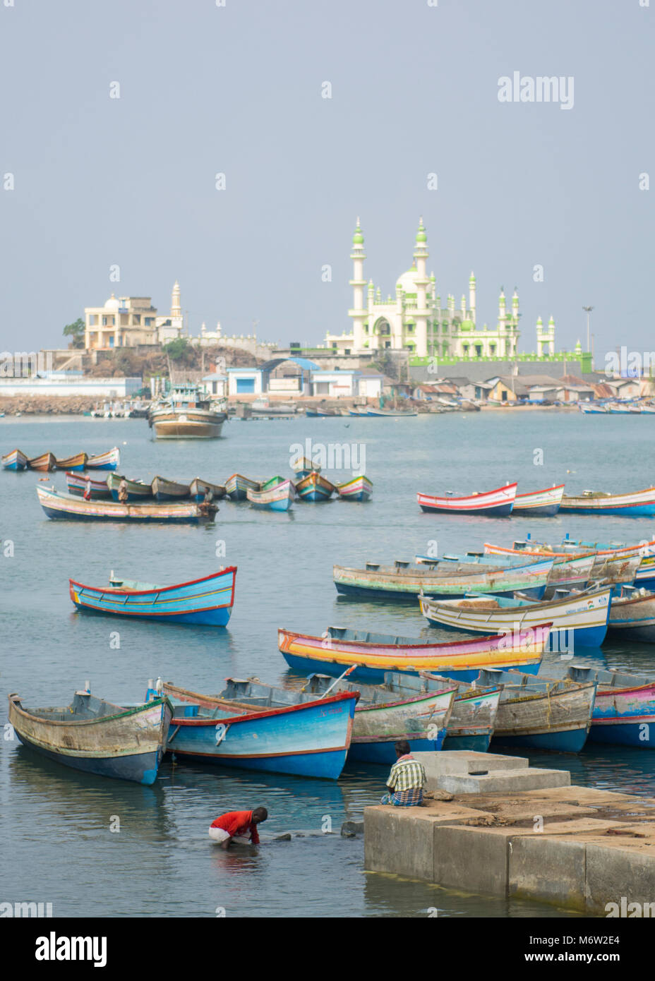 Colourful painted fishing boats with fishermen in foreground and mosque in the background in Vizhinjam Fishing Village Port, Kerala, India Stock Photo