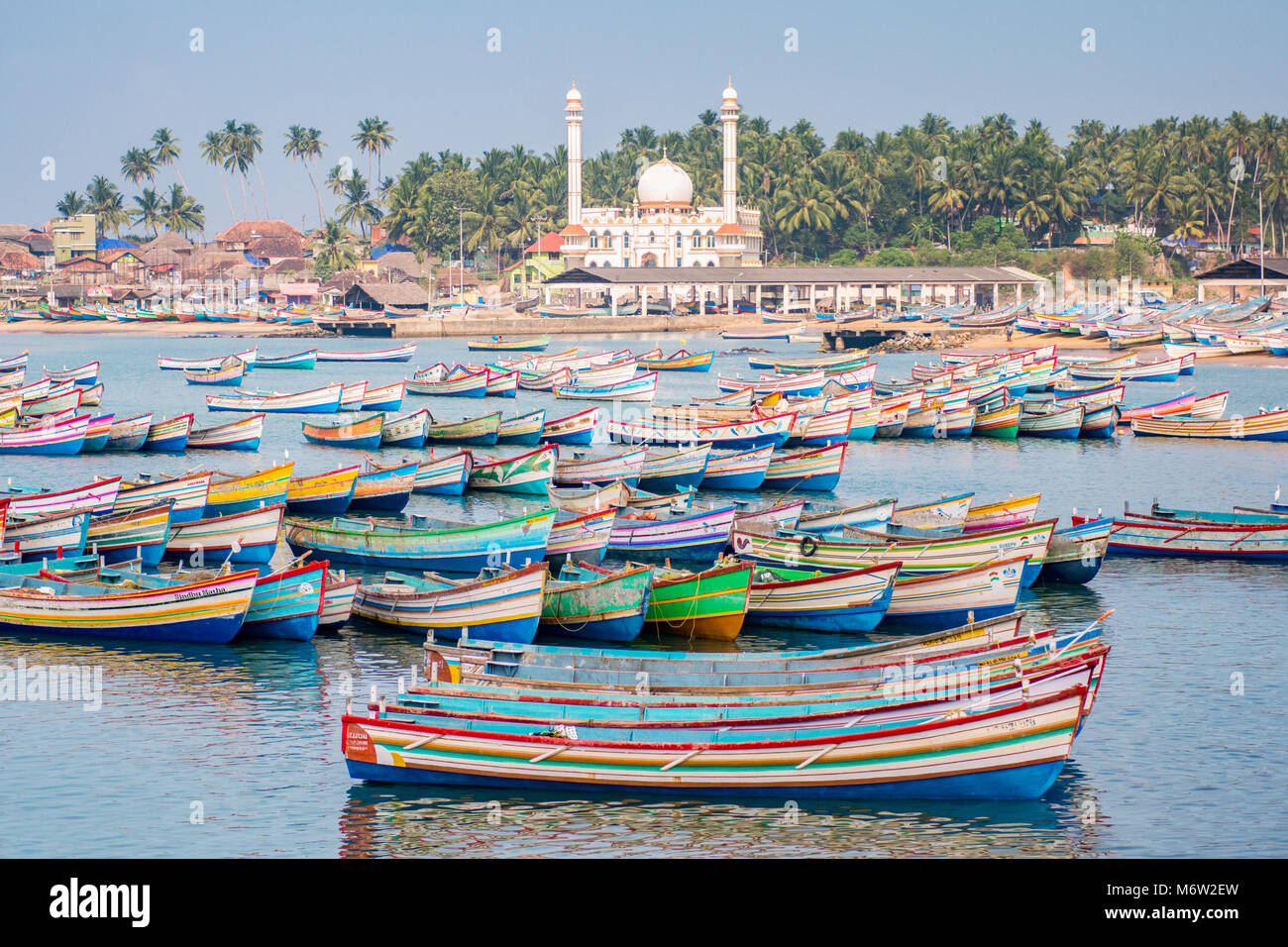 Colourful painted fishing boats with mosque in the background in Vizhinjam Fishing Village Port, Kerala, India Stock Photo