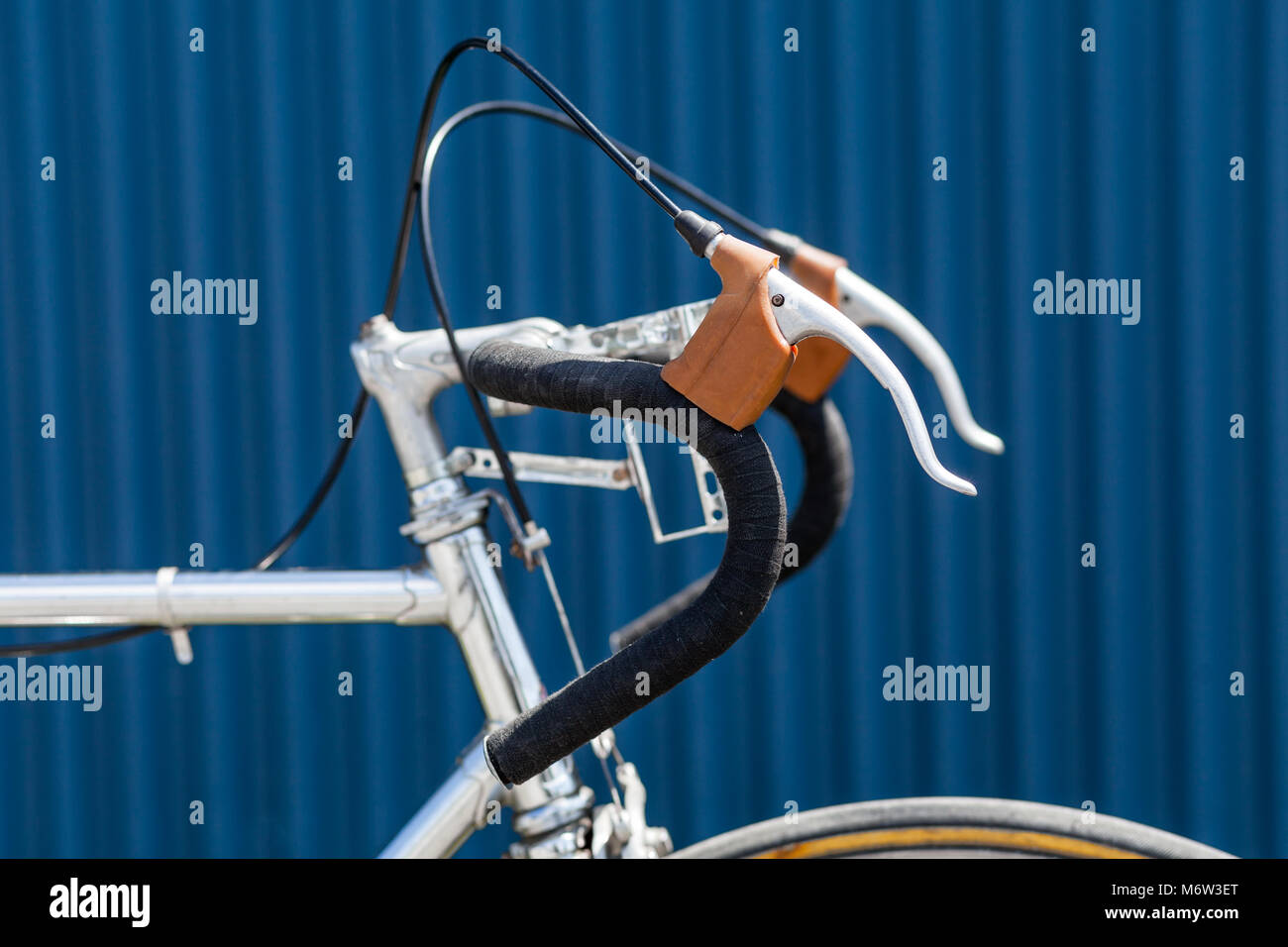 Handlbars with black tape and brake levers of old racing bicycle with chrome frame in front of blue wall Stock Photo