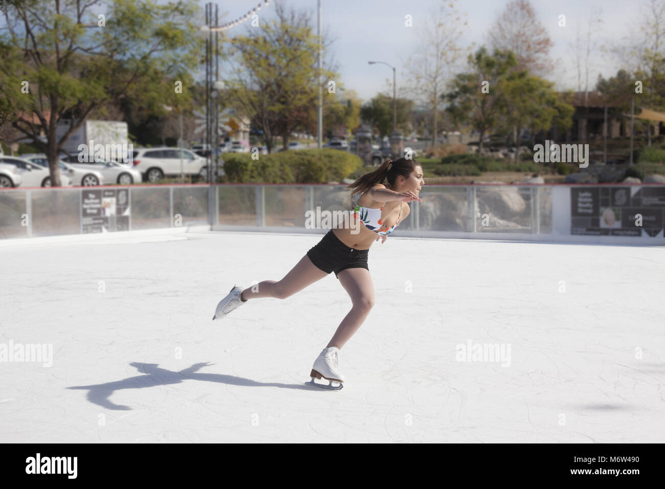 Teenage girl ice skating outdoors in shorts and a bikini top in Southern Califiornia in 85 degree winter weather Stock Photo