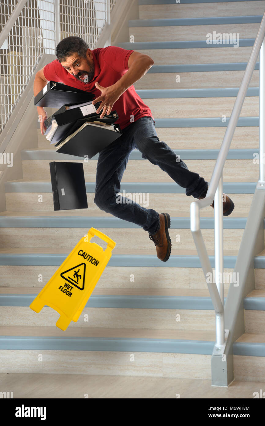 Hispanic worker carrying files falling on wet stairs Stock Photo