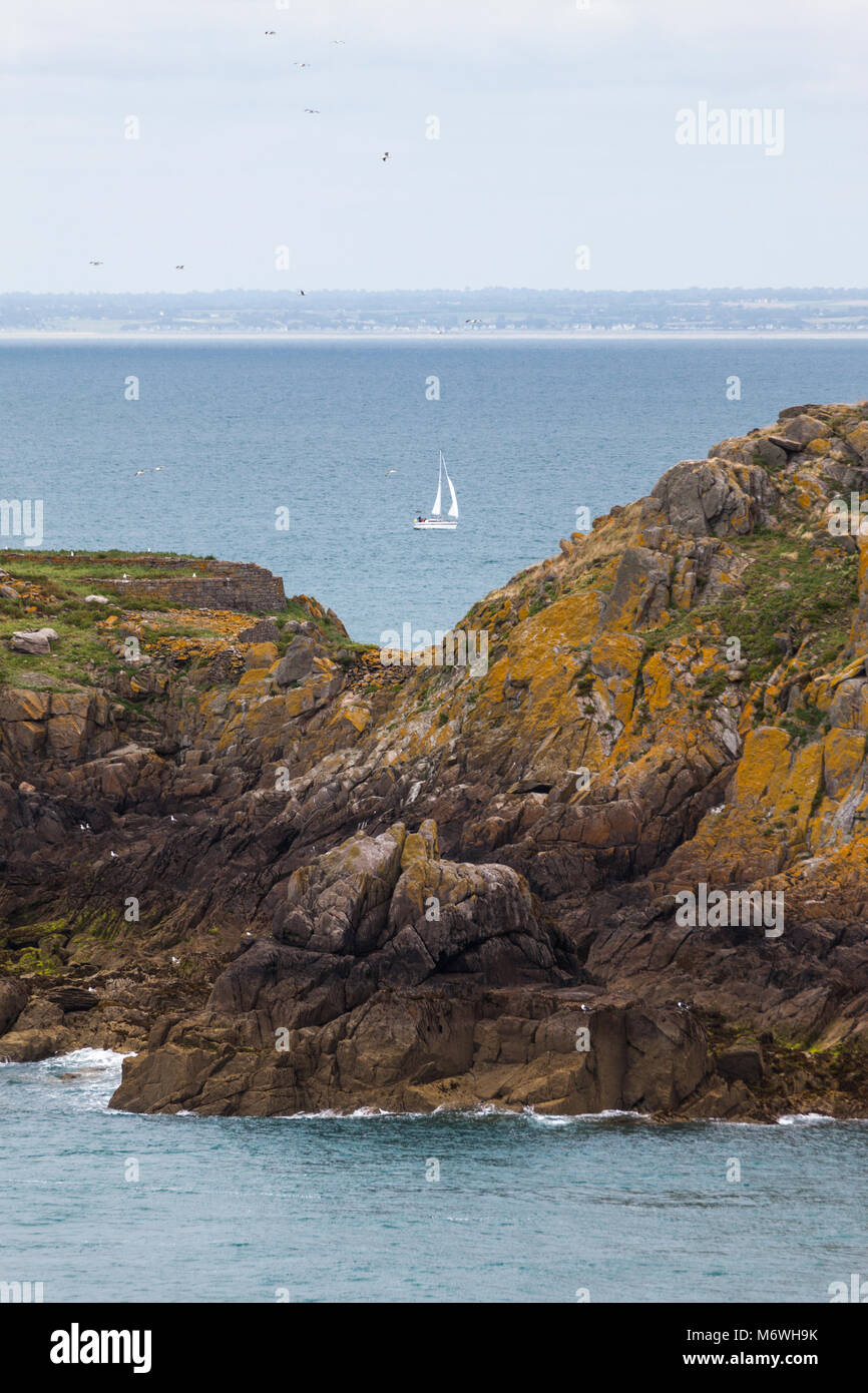 Sailboat with two sails behind the brown rock on ope waters of Bretagne ...