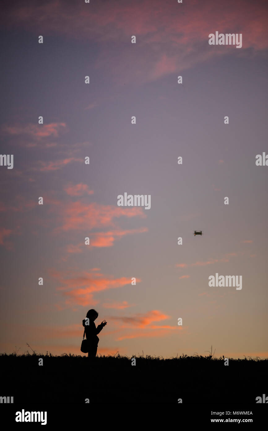 This is the picture of a girl flying her drone outside during sunset. Stock Photo