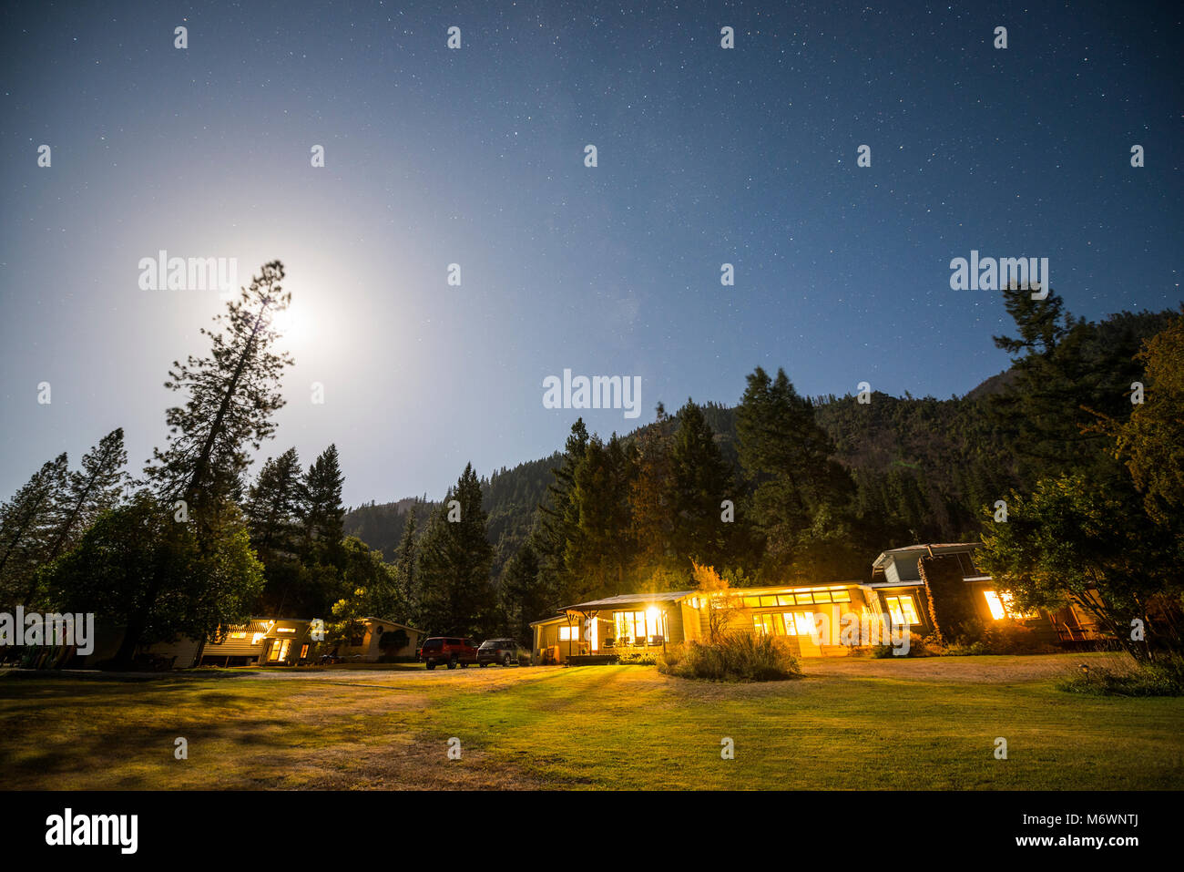 The Otter Bar Lodge and Kayak School is illuminated at night under a full moon with stars in the sky in Forks of Salmon, California. Stock Photo