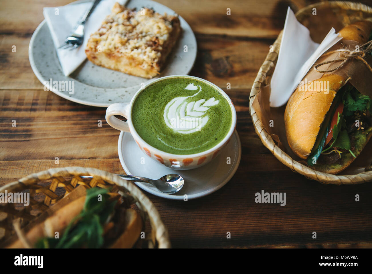 Healthy breakfast in the restaurant: cup of green tea with milk, dessert and sandwiches with vegetables and herbs on wooden table. Stock Photo