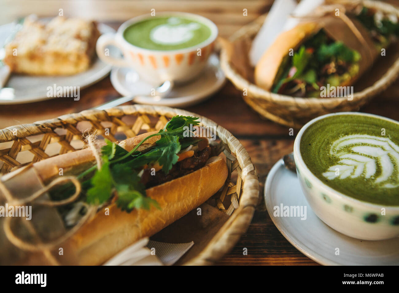 A lot of different food on the table. Healthy breakfast in the restaurant: cups of green tea with milk called Matcha, dessert and sandwiches with vegetables and herbs on wooden table. Stock Photo