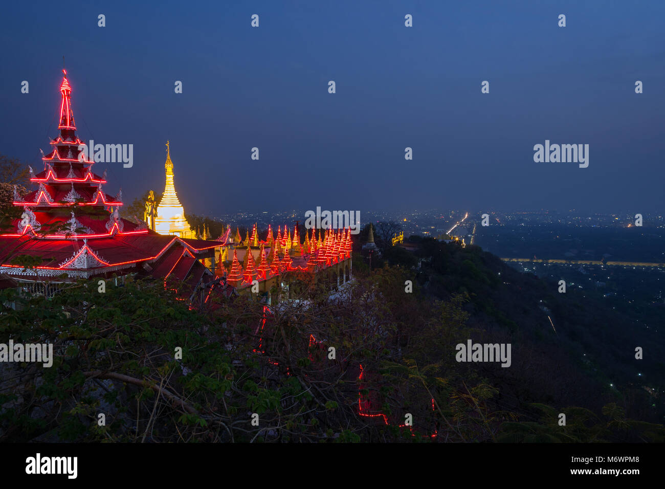 Panoramic view of lit pavilion and golden stupa at the Mandalay Hill and the city below in Mandalay, Myanmar (Burma) in the evening. Copy space. Stock Photo