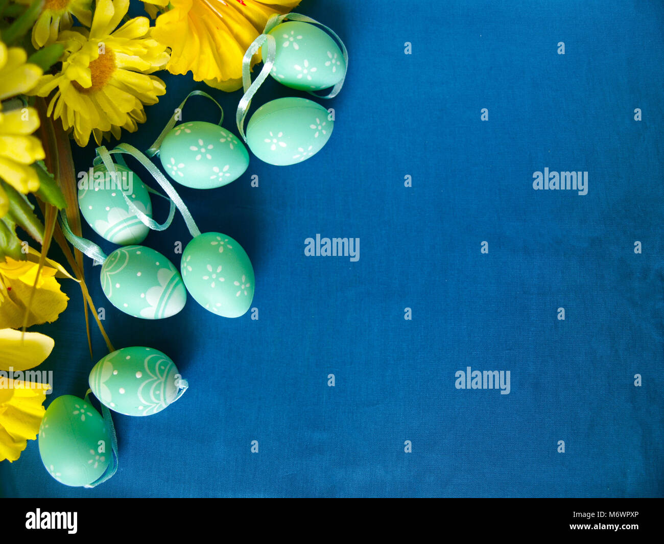 Easter eggs on blue silk, with yellow flowers. Empty space for text. Stock Photo