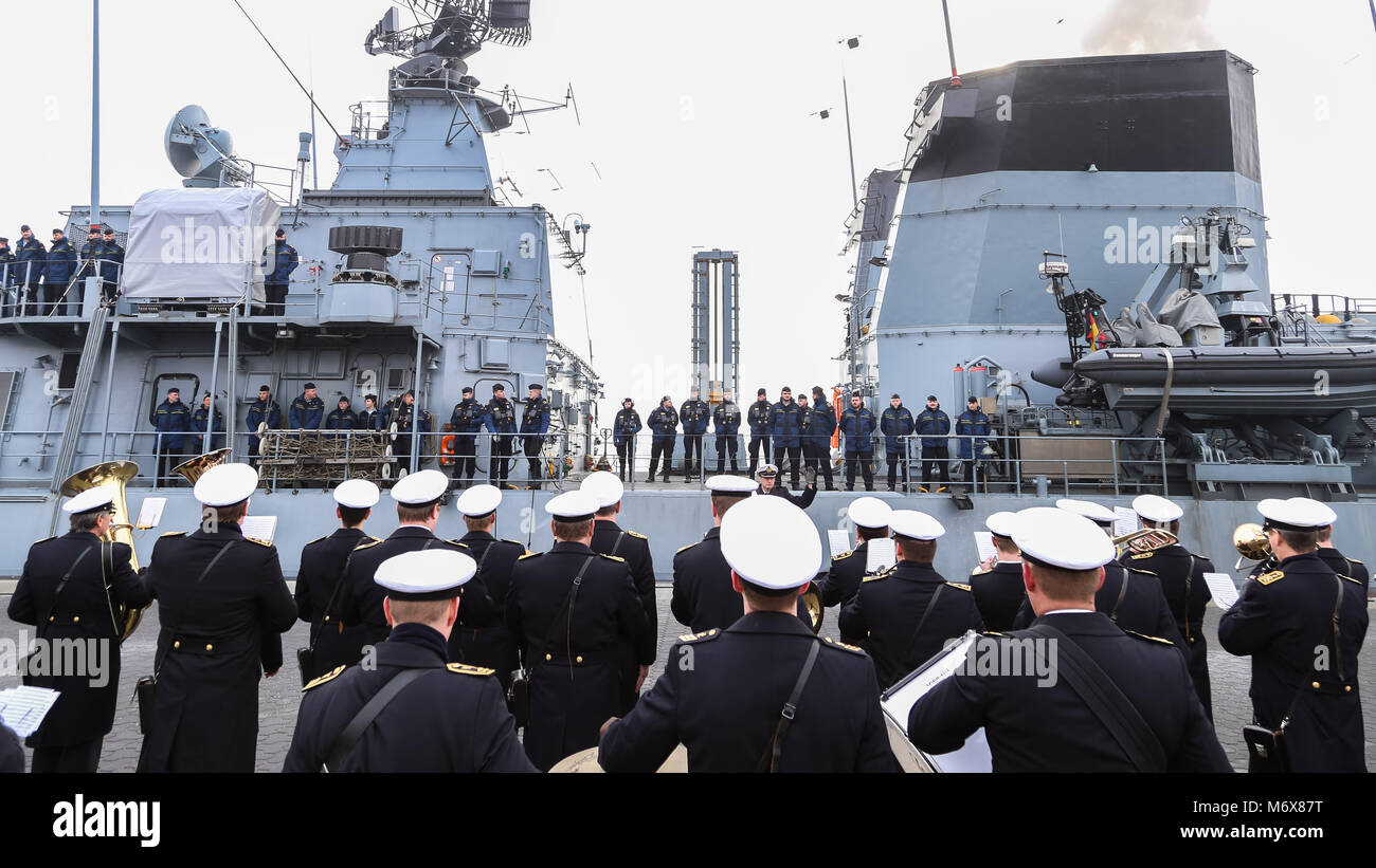 Wilhelmshaven, Germany. 07 March 2018, Navy troops stand attention onboard the German Navy frigate 'Bayern' as a navy brass orchestra (front) plays a serenade on departure of the vessel from the navy base. The 'Bayern' is setting sail for a six-months lasting Nato deployment in the Aegean Sea. Photo: Mohssen Assanimoghaddam/dpa Stock Photo