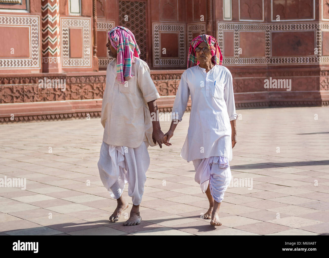 Two men wearing dhotis and kurta holding hands at gateway to the Taj Mahal, Agra, India Stock Photo